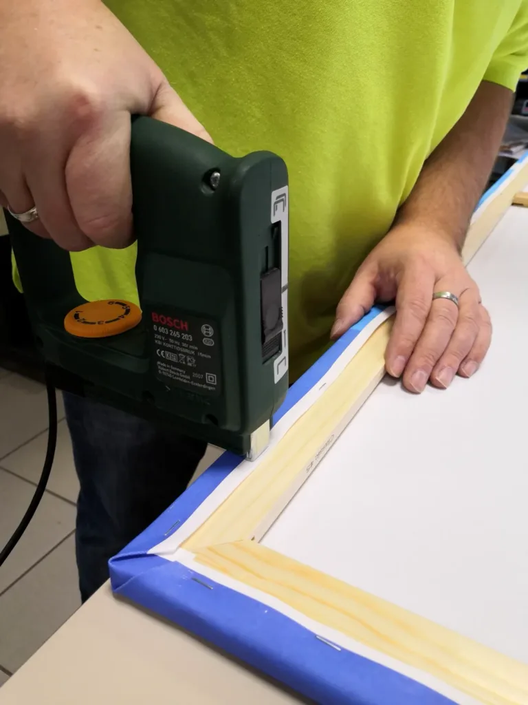 Chef befestigt eine bedruckte Leinwand mit einem Elektrotacker auf einem Holzkeilrahmen
