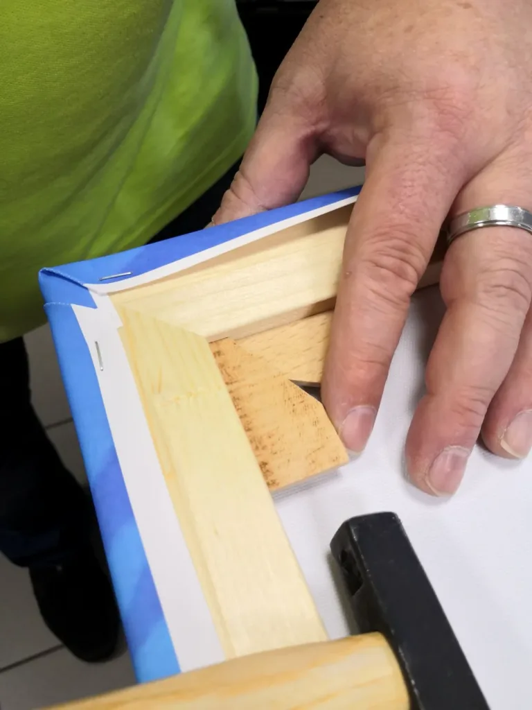 Chef faltet und befestigt die Ecke einer Leinwand auf einem Holzkeilrahmen